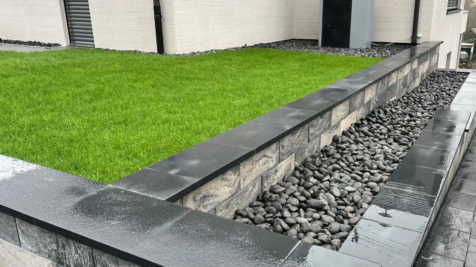 Neu angelegte Rasenfläche mit Natursteinmauer, Kiesstreifen und Terrasse in Siegen