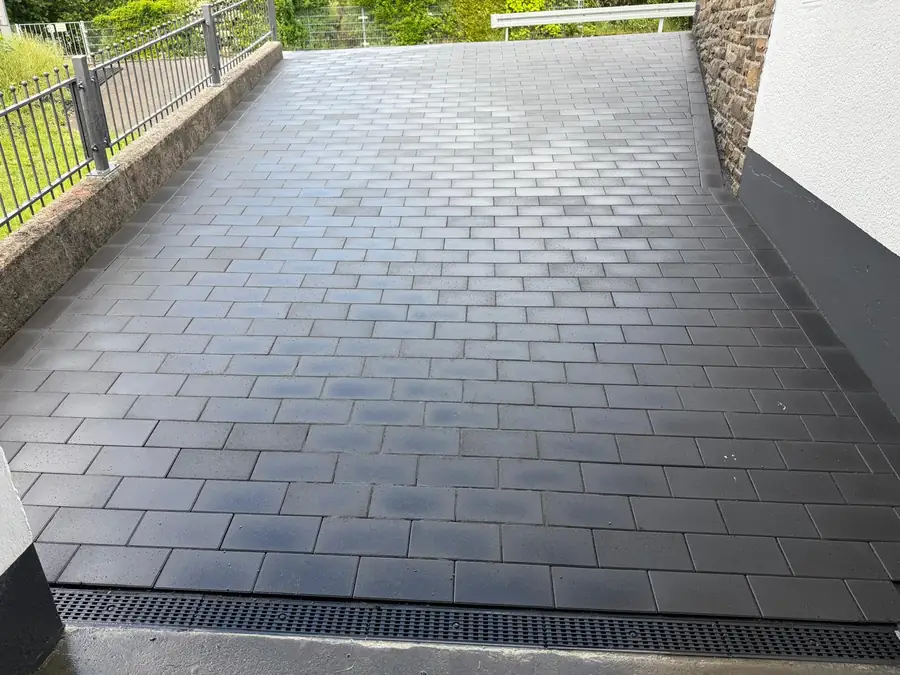 Neu gepflasterte Einfahrt aus dunklem Betonpflaster mit Entwässerungsrinne